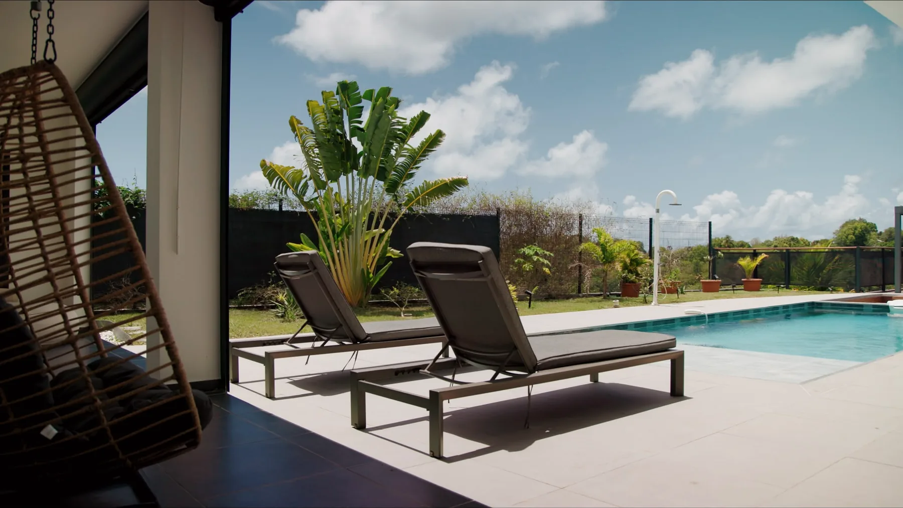 Fauteuil suspendu sur la terrasse couverte, face à la piscine