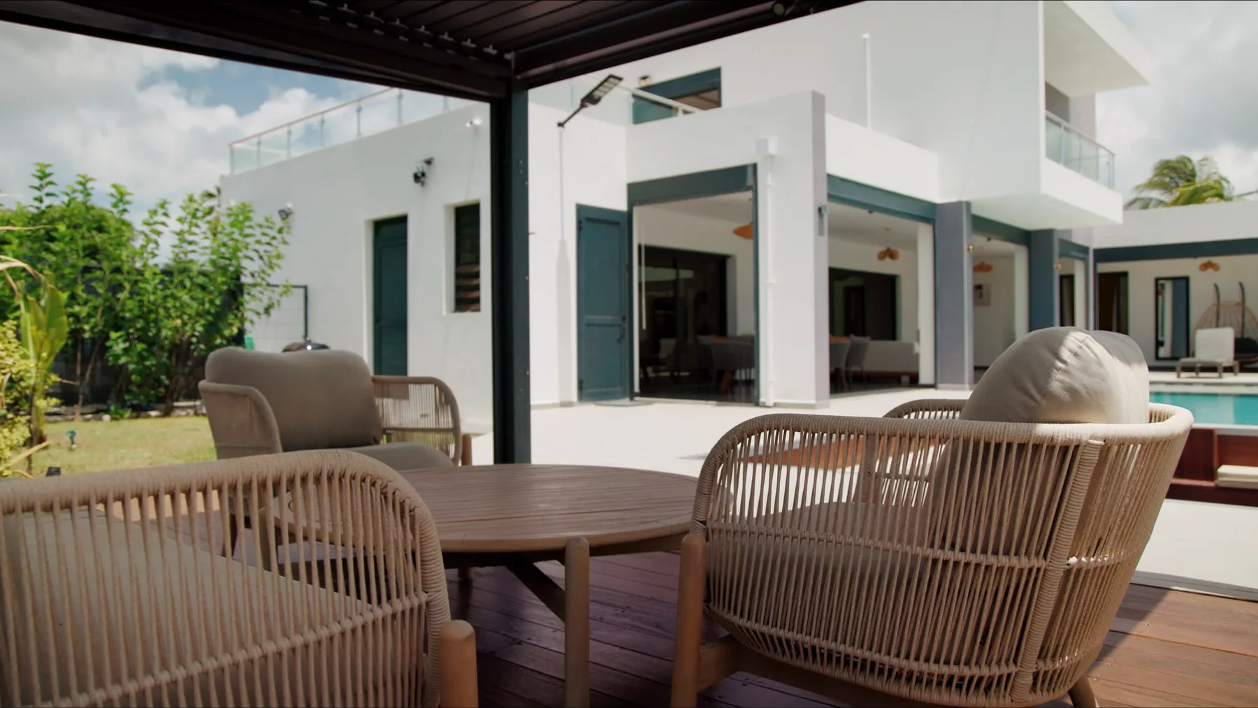 Salon de terrasse en bois exotique sous la pergola, ouvert sur la villa